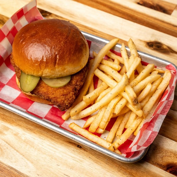 Jaxx Wing Co's fried chicken sandwich with pickles and a side of seasoned fries on a metal tray.