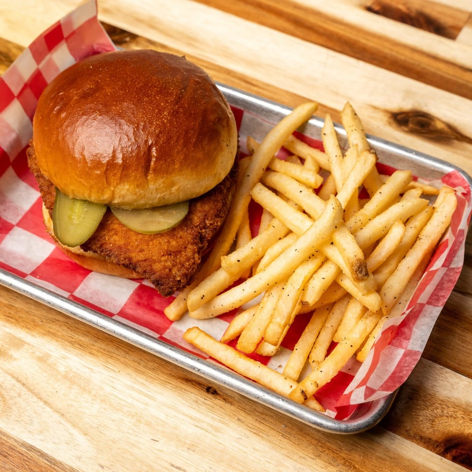 Jaxx Wing Co's fried chicken sandwich with pickles and a side of seasoned fries on a metal tray.