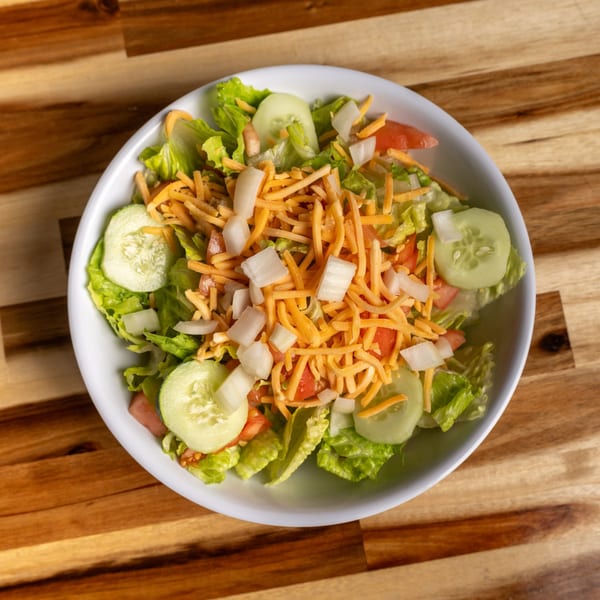 A fresh side salad with lettuce, tomatoes, cucumbers, shredded cheese, and diced onions.