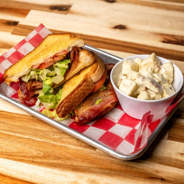 A BLT sandwich with crispy bacon, lettuce, and tomato, served with a side of potato salad.