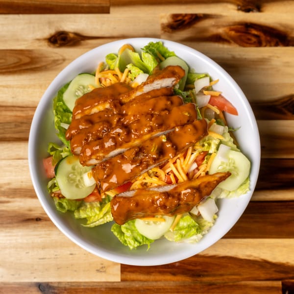 A Jaxx Wing Co. chicken salad with crispy chicken strips, lettuce, cucumbers, tomatoes, and cheese.