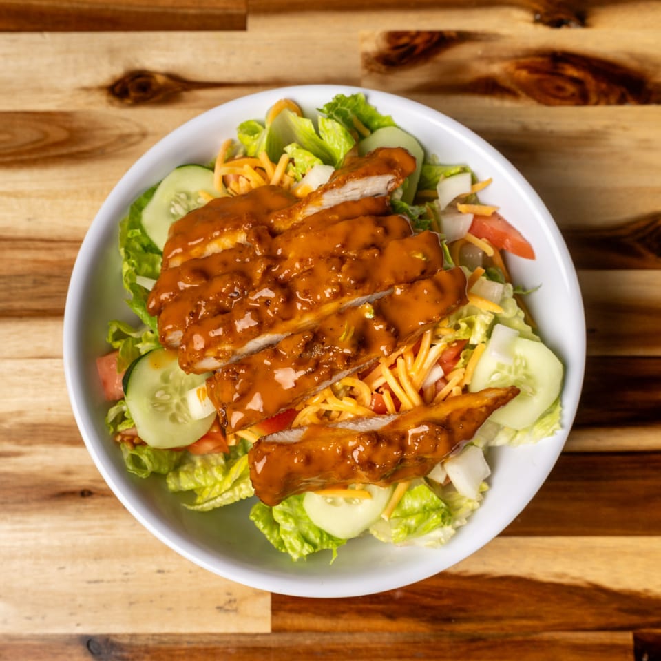 Top-down view of a Jaxx Wing Co. salad with sliced chicken, lettuce, cucumbers, tomatoes, and cheese.