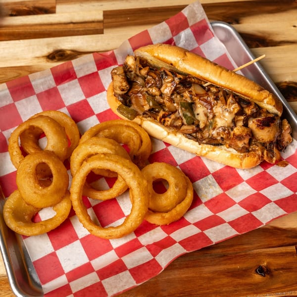 Jaxx Wing Co's cheesesteak sandwich with melted cheese, onions, and peppers, served with golden onion rings.